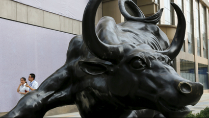 People walk past a statue of bull in front of an investment company at a financial district in Beijing.
