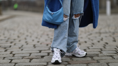 A woman carries a baby blue Prada bag and wears a blue Max Mara coat, baggy Zara jeans, and New Balance sneakers