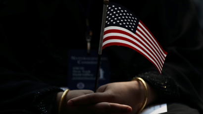 An immigrant woman holds a U.S. flag during a U.S. Citizenship and Immigration Services Naturalization ceremony in the New York Public Library in New York