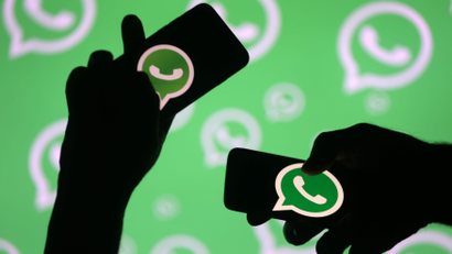 Men pose with smartphones in front of displayed Whatsapp logo in this illustration