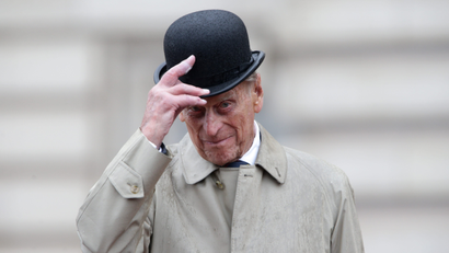 Prince Phillip in a trench coat tipping his bowler hat
