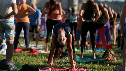 A woman does a backbend surrounded by people arching their backs in a large outdoor yoga class.