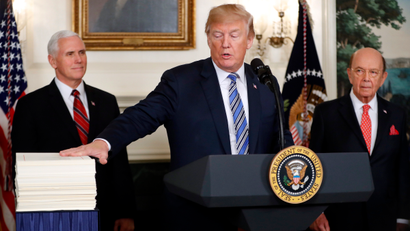 President Donald Trump reaches to touch a copy of the $1.3 trillion spending bill as he speaks in the Diplomatic Room of the White House in Washington, Friday, March 23, 2018. With Trump are Vice President Mike Pence, left, and Commerce Secretary Wilbur Ross.