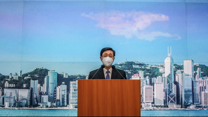 A candidate for Hong Kong chief executive stands at a podium in front of a blue background.