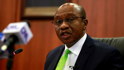 A picture of Nigeria's central bank governor Godwin Emefiele speaking about something, while wearing a black suit, white shirt and a very on-brand lemon-green tie