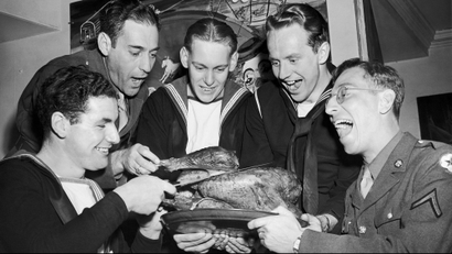 British Seaman J. Webb, left, carves a thanksgiving Day turkey at the American Theatre Wing State Door Canteen in New York, Nov. 26, 1942, as left to right are: Pvt. Sam Fox, U.S. Army; Seaman P. Gimblen, British Royal Navy; Seaman Henry Ward, U.S. Navy, (Home: Omaha, Neb.) and Pvt. Chester Rzezniczek, U.S. Army, (Home: Chicago, Ill.) wait for their servings. (AP Photo)