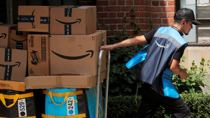 An Amazon delivery worker pulls a delivery cart full of packages.