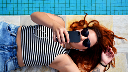 girl laying on her back and holding a cell phone next to a pool