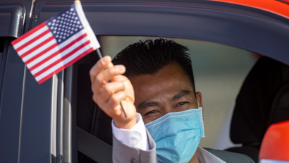 A man waves a U.S. flag after being sworn-in as a U.S. Citizen by a U.S. immigration officer at an empty parking lot during the outbreak of the coronavirus disease.