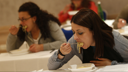 Two women are seen eating pasta.