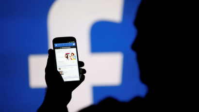 A man is silhouetted against a video screen with a Facebook logo.