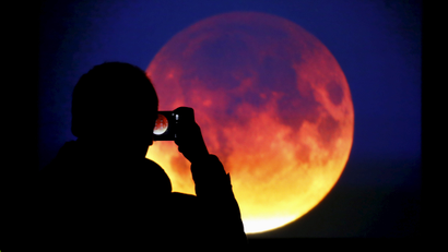 A man takes picture of the screen displaying the moon, appearing in a dim red colour, which is covered by the Earth's shadow during a total lunar eclipse in Warsaw, Poland September 28, 2015.