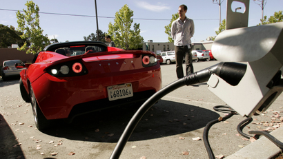 A man charges a red Tesla at an electric charging station in California.