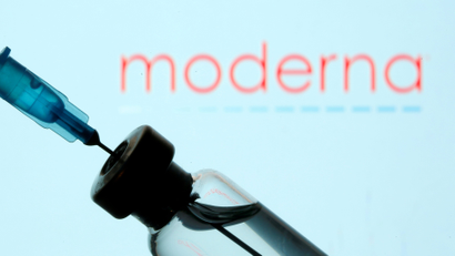 A needle going into a glass vaccine vial in front of the logo for Moderna