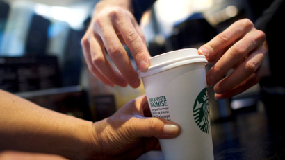 A Starbucks barista putting lid on coffee cup, as someone holds it.