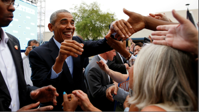 President Obama grins as he shakes the hands of supporters in a massive crowd.