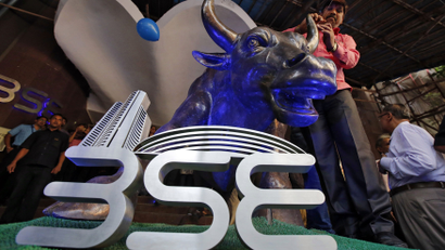 A man ties a balloon to the horns of a bull statue at the entrance of the BSE while celebrating the Sensex index rising to over 30,000, in Mumbai