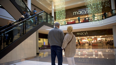 A couple holds hands in front of a Macy's store in a mall