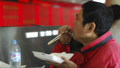 An investor eats before an electronic board in a brokerage hall in Shanghai April 24, 2008. China's main stock index soared over 7 percent in frenzied trade on Thursday after the government cut the share trading tax, seeking to end a bear market that had slashed stock prices by half in six months.