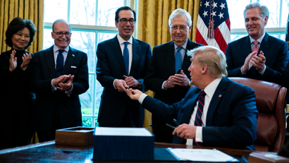 President Donald Trump hands a pen Treasury Secretary Steven Mnuchin, after signing the coronavirus stimulus relief package in the Oval Office at the White House, Friday, March 27, 2020, in Washington. From left, Secretary of Transportation Elaine Chao, White House chief economic adviser Larry Kudlow, Mnuchin, Senate Majority Leader Mitch McConnell of Ky., Trump, and House Minority Leader Kevin McCarty, R-Calif.