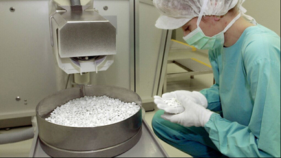 A scientist wearing a mask and gloves as she counts pills in a basin in a lab setting.