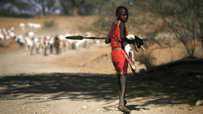 A young Maasai herder carries a kid that is too weak to walk on the road to Pakase village