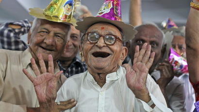 An elderly gentleman and his friends smile while wearing party hats at a celebration