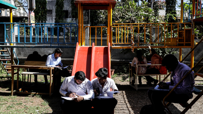 Job seekers fill up their forms while sitting on swings before lining up for interviews at a job fair in Chinchwad