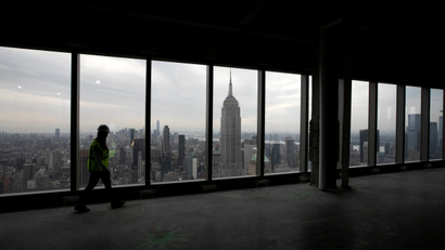 A person walks through an empty floor of an office tower in New York City that faces the Empire State Building, framed in the center of a window.