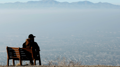 A man sits on a park bench and looks over the smog filled Salt Lake Valley in Draper, Uta