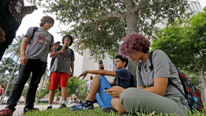Pokemon Go players Ana Valentina Ojeda, right, and Jaeden Valdespino, second from right, check their smartphones as they look for Pokemon, Tuesday, July 12, 2016, at Bayfront Park in downtown Miami. The "Pokemon Go" craze has sent legions of players hiking around cities and battling with "pocket monsters" on their smartphones. (AP Photo/Alan Diaz)