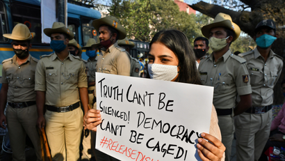 A woman holds a placard next to policemen during a protest against the arrest of climate activist Disha Ravi, in Bengaluru, India