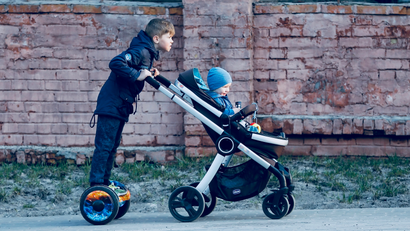 A young boy carries a baby carriage with his brother as he rides a gyroscooter in downtown Kiev, Ukraine.