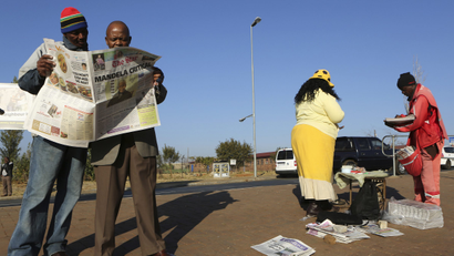 Men read a newspaper next to a stall in Soweto