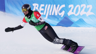 A US athlete on a snowboard celebrates in front of a blue logo for the Beijing Olympics.