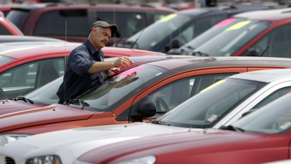 A worker paints price tags in the used car lot at a Chrysler car dealership