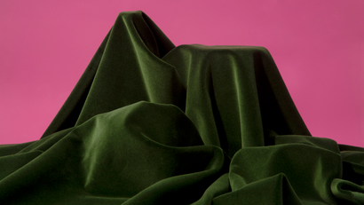 An emerald green cloth draped over objects, concealing them entirely, set against a magenta background.