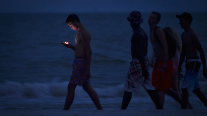 A person looking at their cell phone while they walk on the twilight beach.