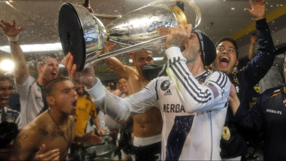 David Beckham celebrating in a locker room, drinking champagne out of a trophy.