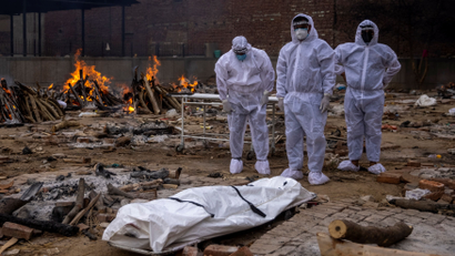 Men wearing protective suits stand next to the body of their relative, who died from the coronavirus disease (COVID-19), before her cremation at a crematorium ground in New Delhi