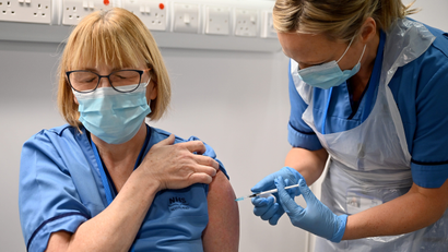 A person receive a Covid-19 vaccine in her upper arm; she and the health care provider are both wearing blue masks.