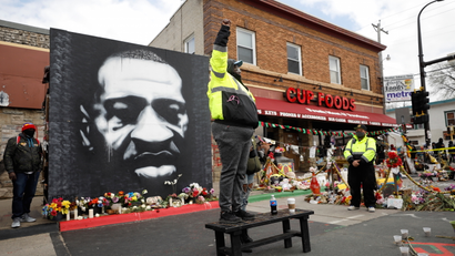 A mural of George Floyd by the Cup Foods store where he was murdered, with a man standing with a raised fist in the foreground