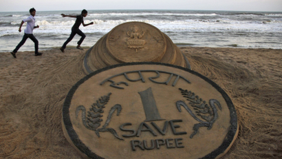 Boys run near a sand sculpture of the Indian Rupee created by Indian sand artist Sudarshan Pattnaik at golden sea beach at Puri