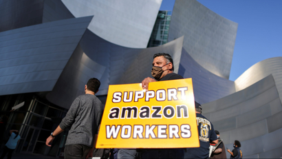 A protestor holds a sign saying "Support Amazon workers" in front of a building in Los Angeles