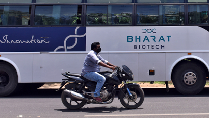 A man rides his motorbike past a parked bus of India's biotechnology company Bharat Biotech outside its office in Hyderabad