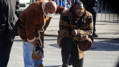 A man bends on one knee while another pats him on the back during a vigil in honor of victims of an apartment building fire in the Bronx, New York city.