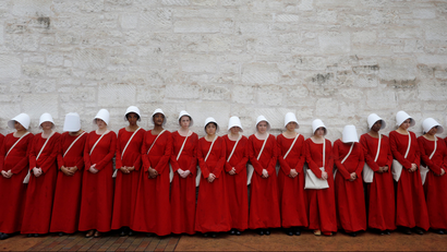 Women dressed as handmaids promoting the Hulu original series "The Handmaid's Tale" stand along a public street