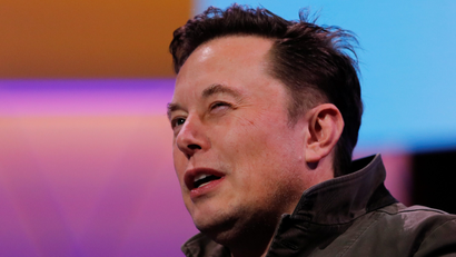 Elon Musk squinting as he speaks on stage.