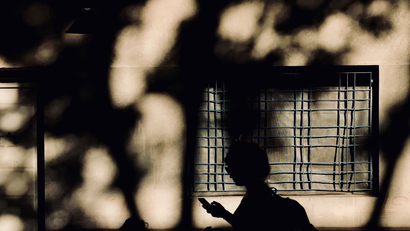 A woman is silhouetted as she looks at her cell phone.