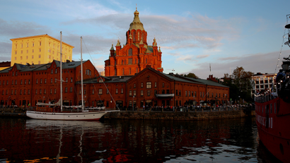 An ornate red cathedral rises into the evening sky above a placid waterway